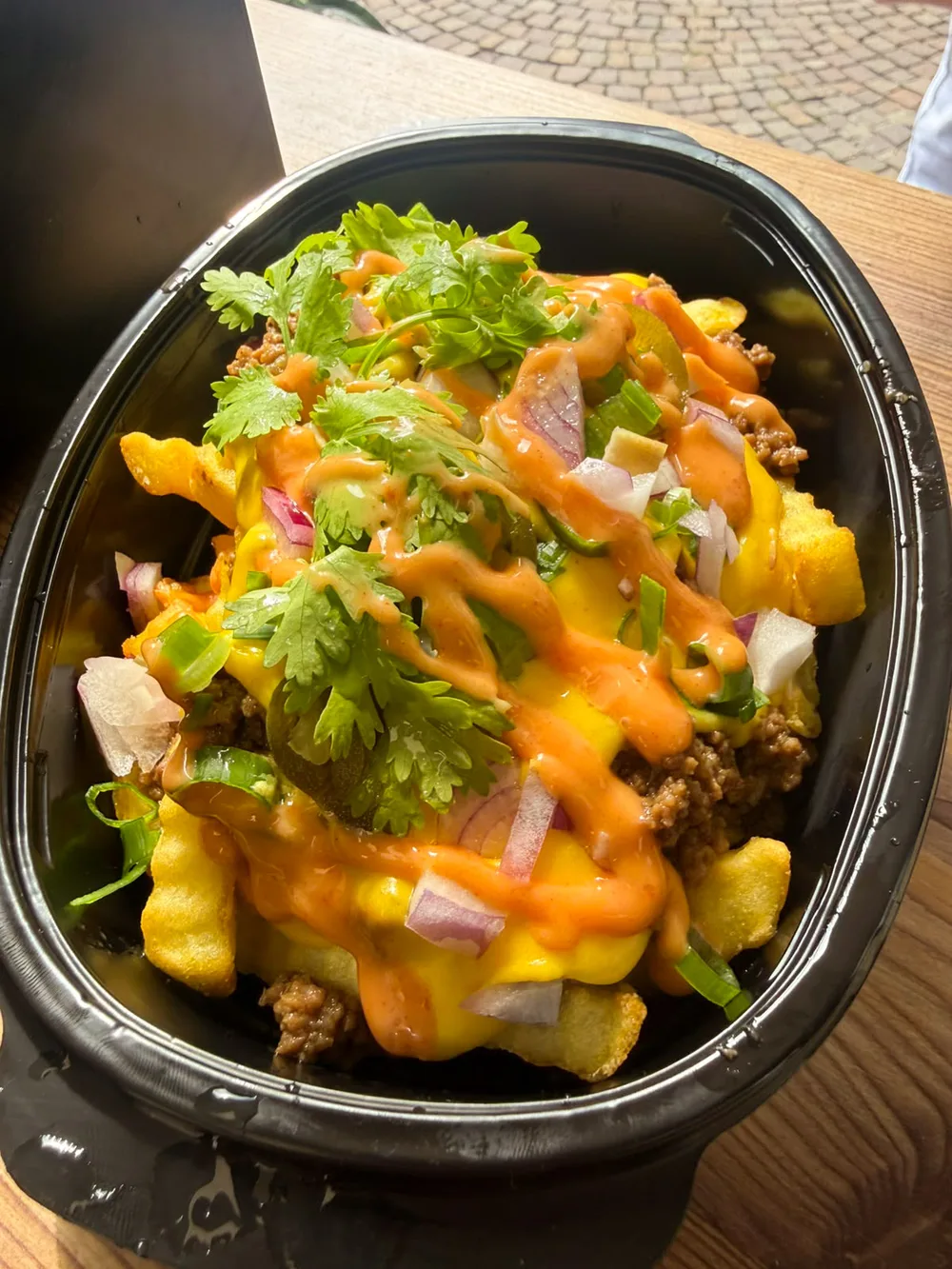 Loaded Fries mit Hackfleisch, Käsesauce, Sriracha-Mayo, roten Zwiebeln und Koriander in einer schwarzen Schale