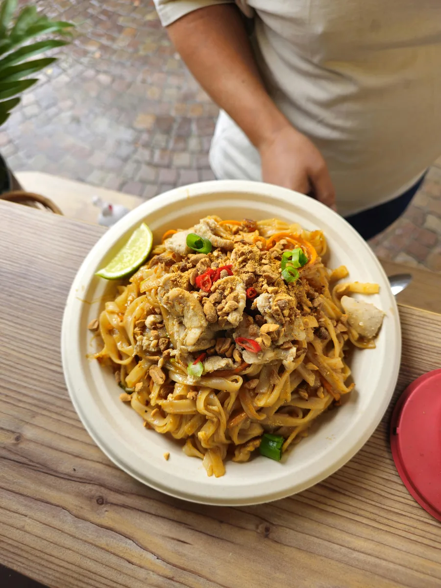 Pad Thai mit Erdnüssen, Chilischeiben und Limette in einer Takeaway-Schale am Marktstand