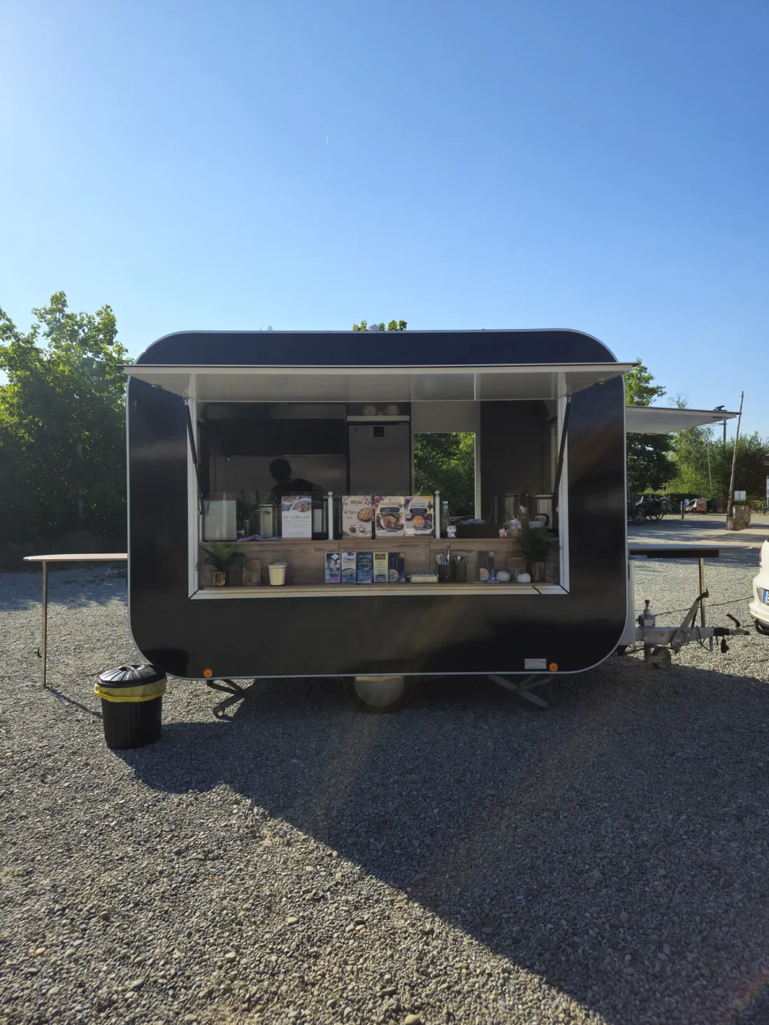 Der schwarze Red-Lotus-Foodtrailer bei Sonnenschein mit geöffneter Verkaufsklappe